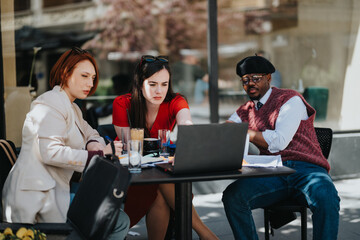 Three focused business partners engaged in a strategic meeting outdoors, discussing over laptops and notes.