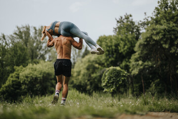 Man carrying his girlfriend over his shoulders in a playful manner in a lush green park. Capturing...