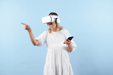 Caucasian girl wearing VR glasses while holding phone and pointing at view. Happy woman surprised...