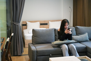 Obraz premium Women using smartphone and sitting on sofa in living room at home, interior, life style.