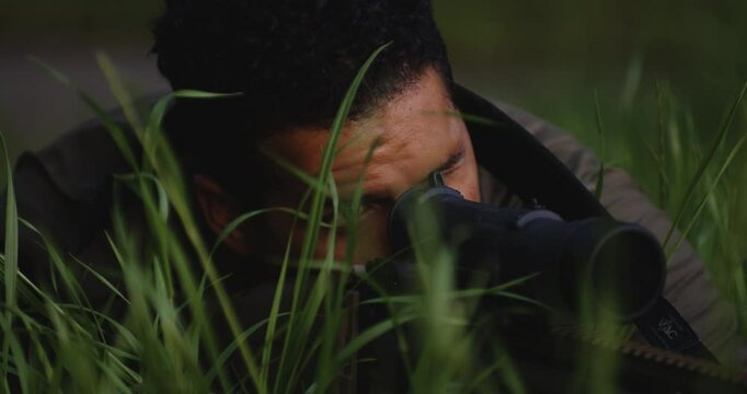 Deadly precision - stealthy sniper aiming its target while hiding in grass.