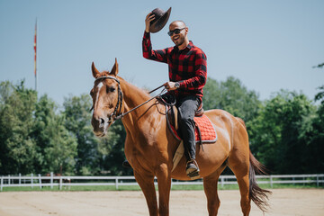 Smiling man in checked shirt tips hat while riding a horse outdoors on a sunny day, exuding joy and...