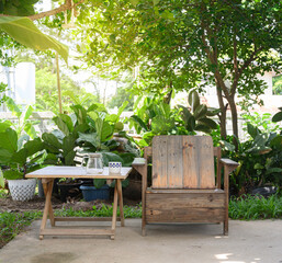 The chair and table wood is positioned under the shade of a tree, surrounded by lush green plants and foliage.