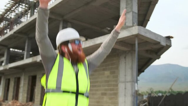 Construction worker at construction site dancing with hands up and enjoy moment end of work shift in uniform and safety helmet.