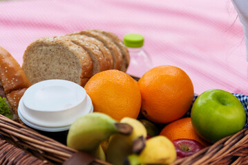 Picnic basket food bread fresh fruit coffee cup orange juice in wood wicker box on red Blanket. Wheat bakery fruit food and drinks in green park outdoor lifestyle. Breakfast healthy appetizer box.