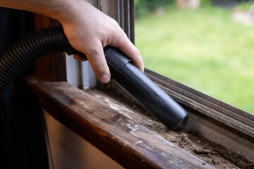 Cleaning debris out of window ledge and grooves with vacuum.