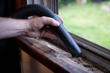 Cleaning debris out of window ledge and grooves with vacuum.