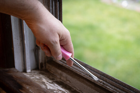 Cleaning debris out of window ledge and grooves with screwdriver tool.