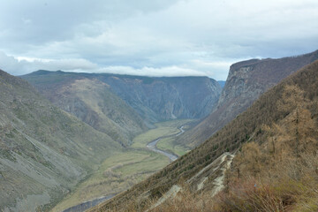 View of a winding river flowing along the bottom of a deep canyon into a steep dirt road descending...