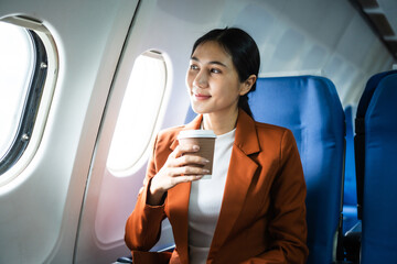 A woman in a formal suit sits in a window seat of an economy class section, looking out the airplane window, ready for her business journey.