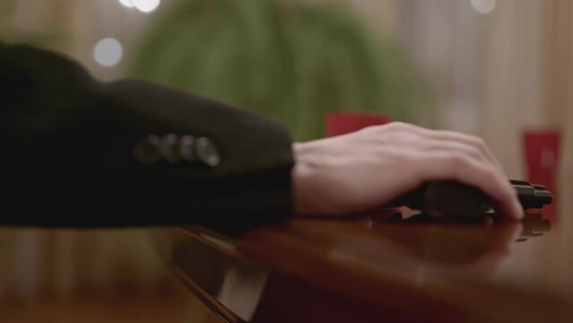 Close-up of thug holding gun. Stock. Man holds gun on table and threatens. Thug threatens with gun at negotiating table