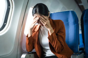 A young Asian woman, an airplane passenger, sits by the window seat, experiencing nausea and...