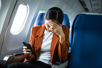 A young Asian woman, an airplane passenger, sits by the window seat, experiencing nausea and...