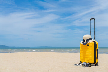 Naklejka premium Suitcase with beach accessories on sand, hat, sunglasses, camera, sea and sky background. summer travel concept.