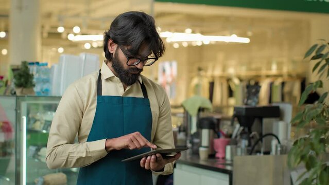 Indian male waiter in cafe working with pc using internet service writing client order in digital tablet cafeteria worker Arabian barista man managing online menu on wireless computer small business