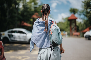 A woman with braids and a backpack walking in a parking area with trees and a clear sky. Outdoor activity and exploration.