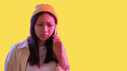 Phone problem. Mobile scam. Pink neon light skeptic frowning woman using gadget with bad connection isolated on yellow empty space background.
