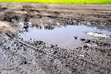 Selective focus on mud and torn up grass in the foreground of a dirt parking lot