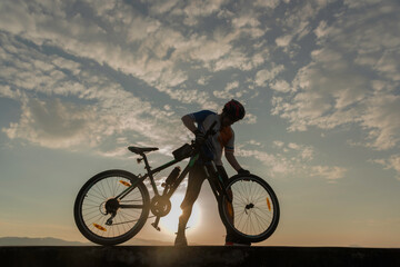 Man cyclist repairing a bike against the background of sky