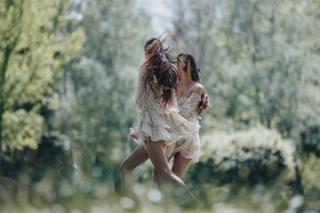 Two young women, dressed in flowing dresses, express joy and freedom as they dance in a lush,...