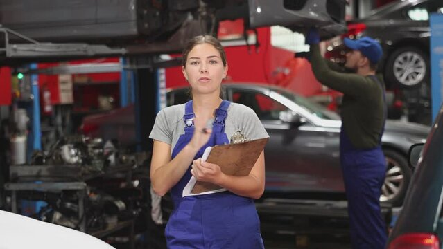 Female car service worker keeps records of work performed by auto mechanics in a car service station - makes notes on paper. High quality 4k footage