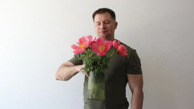 A man in a hacky t-shirt holds a vase of peonies and points to the camera