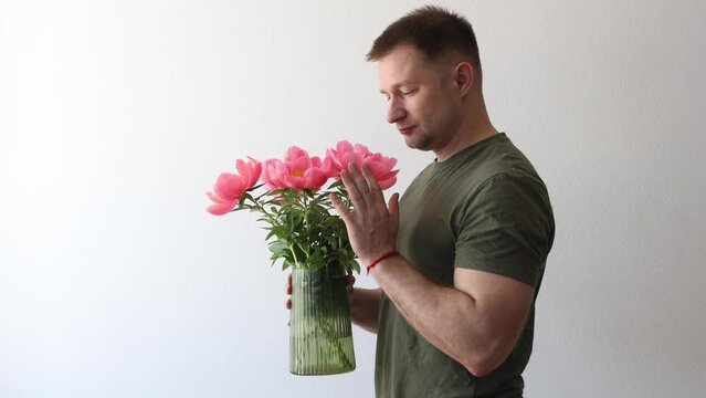 A man in a hacky t-shirt holds a vase of peonies and points to the camera