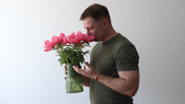 A man in a hacky t-shirt holds a vase of peonies and points to the camera