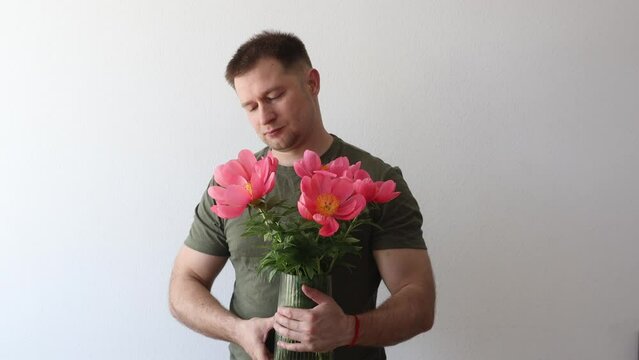 A man in a hacky t-shirt holds a vase of peonies and points to the camera