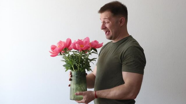 A man in a hacky t-shirt holds a vase of peonies and points to the camera