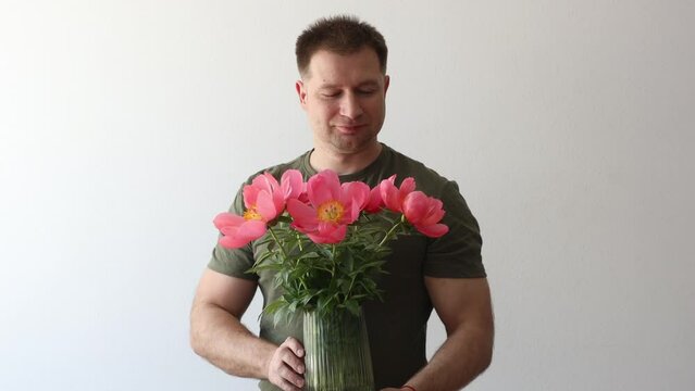 Man in hacky t-shirt holds vase of peonies and points to camera