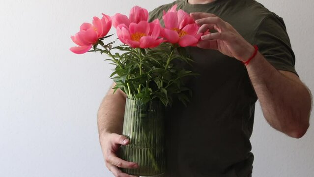 A man in a hacky t-shirt holds a vase of peonies and points to the camera