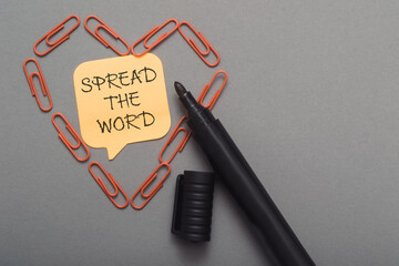 A black pen with a yellow note that says Spread the word
