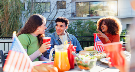 Friends, celebration and independence day outdoor with food, drinks and talking of international holiday. Social group of people by American Flag, barbecue and lunch at patio table for fourth of July