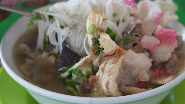 A bowl of Mi sop Medan with yellow noodles, shredded chicken, and green vegetables in a clear broth.