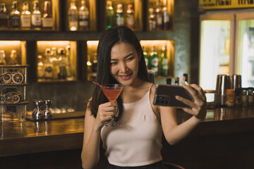 Asian woman taking a photo of herself while drinking whiskey at the bar.