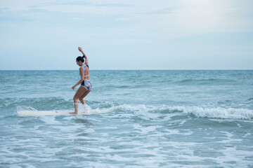 Asian surfing woman riding the waves on sunny day, outdoor activities, water sports activities concept