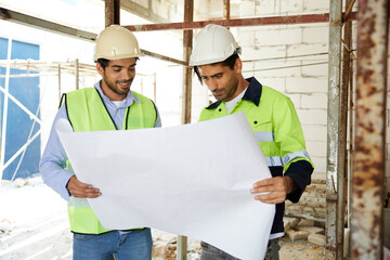 workers or architects holding and reading plan blueprint paper at construction site