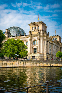 Teilansicht des Reichstagsgeb&auml;udes, im Vordergrund die Spree, leicht bew&ouml;lkter blauer Himmel, vertikal
