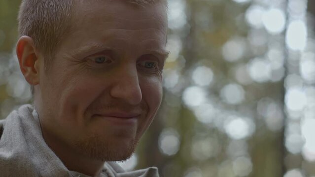 Close-up of man smiling and talking in woods. Stock. Cinematic portrait of man in style of teacher in forest. Man speaks and smiles like sensei