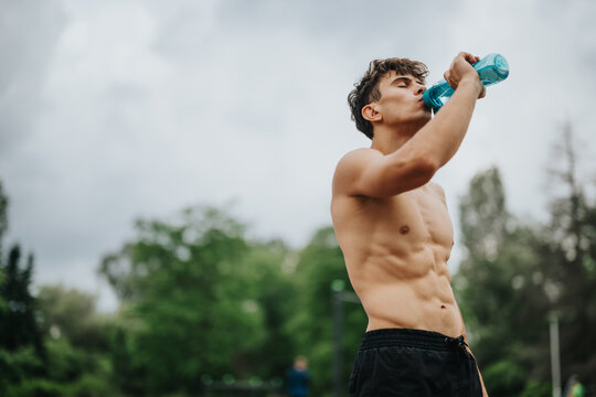 Young athletic man drinking water while exercising outdoors. Staying hydrated and fit during outdoor workout under the cloudy sky.