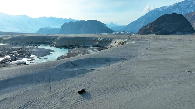 Off-road vehicle traversing Sarfaranga Cold Desert's sandy terrain with snow-capped mountains in the background.