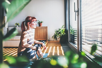 Beautiful redhead woman's home fitness routine. Home workout on gym mt in living room, sporty woman wearing sportswear.