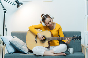 Portrait of young asian woman playing guitar on sofa relaxing stress on vacation.