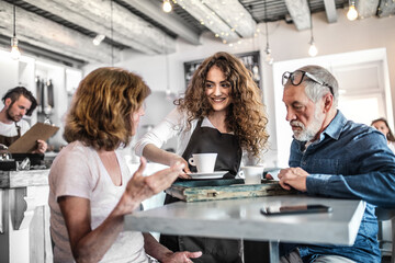 Beautiful female barista working in coffee shop, serving customers, elderly couple. University student working part-time in cafe.