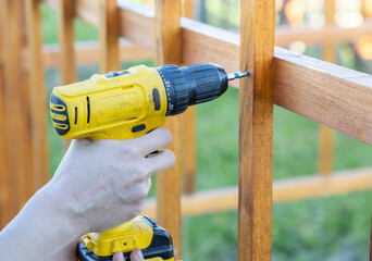 A person in work attire using a power drill to secure a wooden fence panel onto metal posts in a...