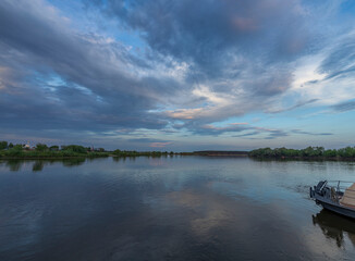 A lone boat peacefully glides along the calm river beneath thick, cloudy skies in the serene ambiance of springtime.