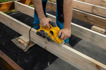 A close-up shot of a carpenters hands using a planer to smooth a wooden beam. The carpenter is...
