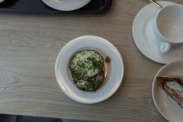 A close-up shot of a plate with two pieces of toasted bread topped with herbs and a small dollop of mustard, accompanied by a sandwich on a separate plate.