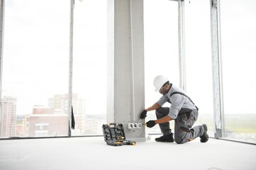 An African electrician installs electrical outlets at a construction site